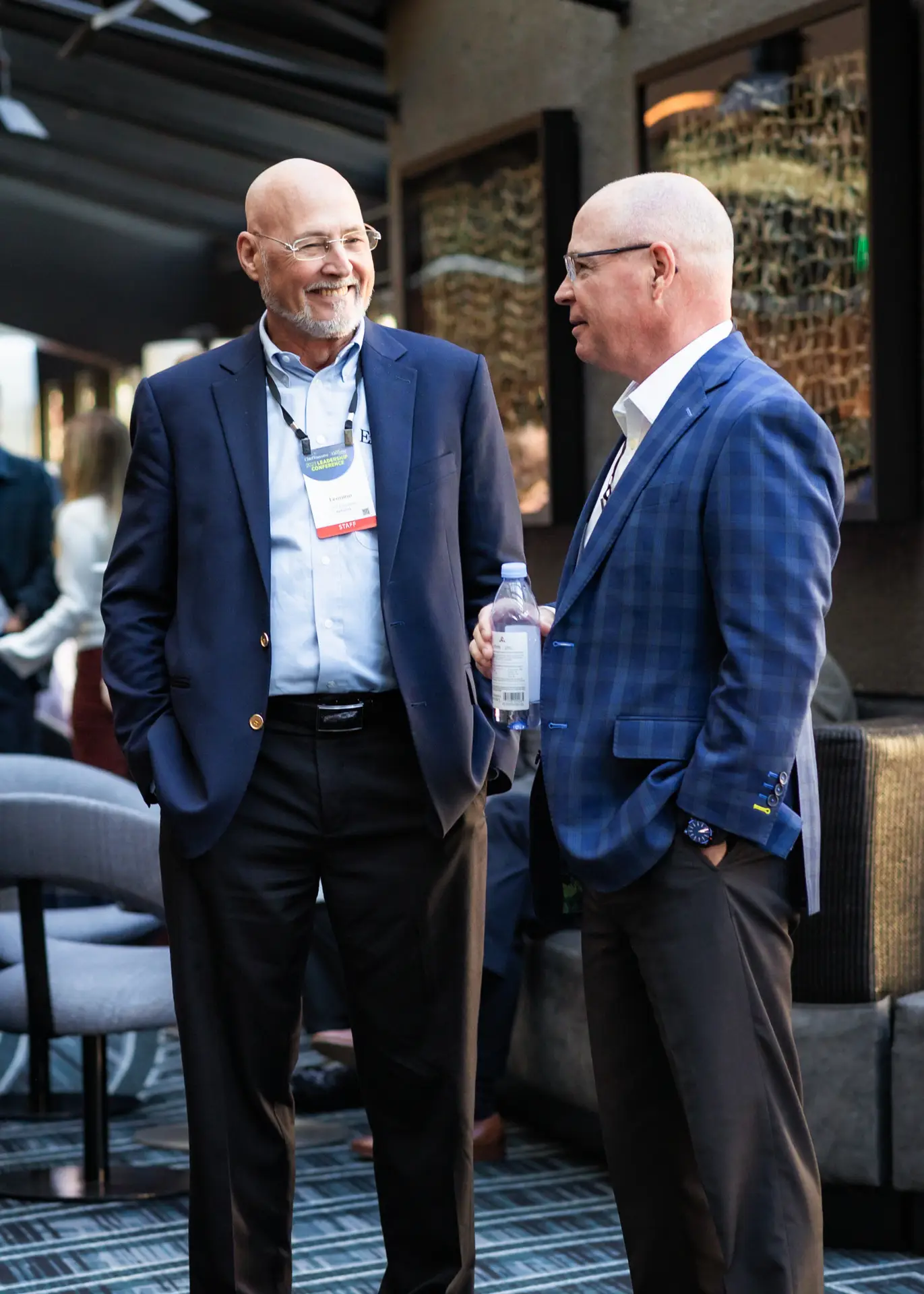 Two men standing and talking to each other. Both are wearing business casual with blazer on.